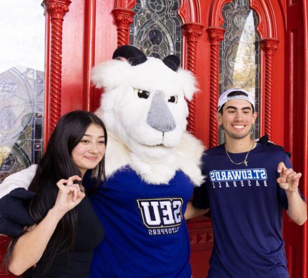 Two students and topper stand outside of the red doors and make toppers up hand signs.